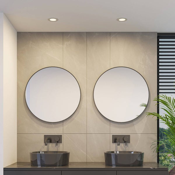 Modernes Badezimmer mit zwei runden Spiegeln, schwarzen Aufsatzwaschbecken und Wandarmaturen vor einer Wand in Steinoptik.