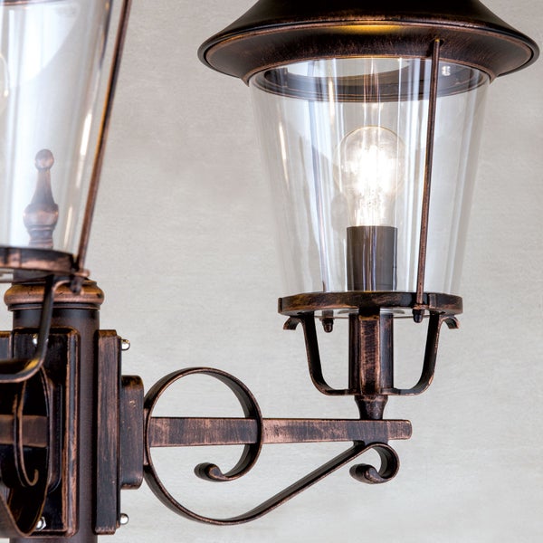 Klassische Außenwandleuchte in Bronze-Optik mit zwei Laternen, klarem Glas und dekorativem Wandhalter aus Metall.