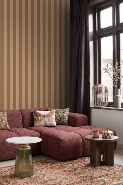 Gestreifte Tapete in Erdtönen hinter einem dunkelroten Polstersofa in einem Wohnzimmer mit Beistelltischen und einem gemusterten Teppich.