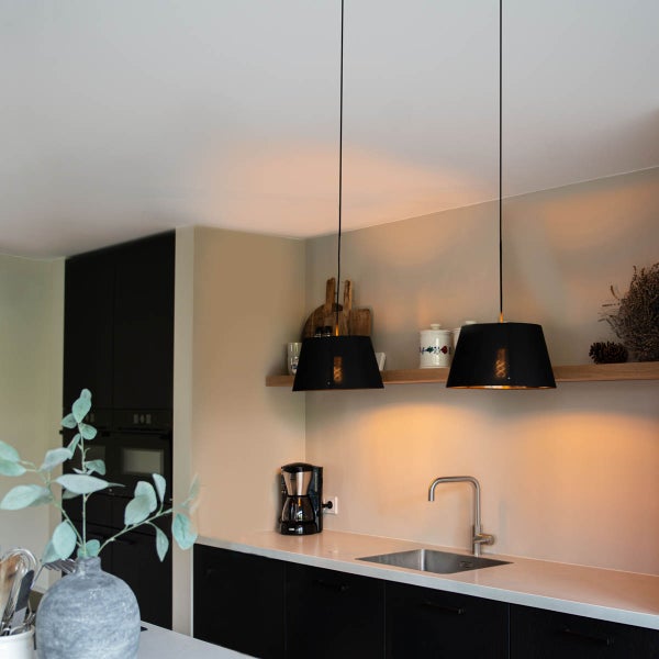 Moderne Küchenszene mit schwarzen Schränken, einer hellen Arbeitsplatte und zwei schwarzen Pendelleuchten über einer Edelstahlspüle.
