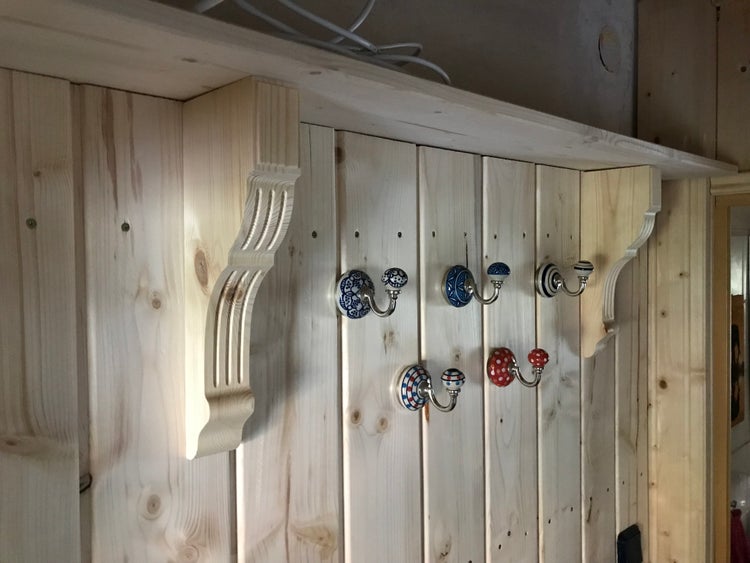 Wandgarderobe aus hellem Kiefernholz mit verzierten Konsolen und verschiedenen dekorativen Kleiderhaken mit Keramikknöpfen.