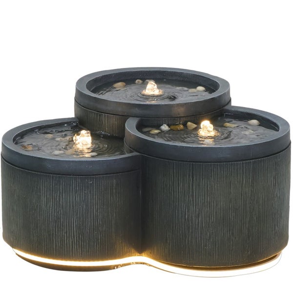 Dreistufiger Gartenbrunnen mit vertikaler Rillenstruktur, integrierter LED-Beleuchtung und sprudelnden Wasserbecken mit Steinen.