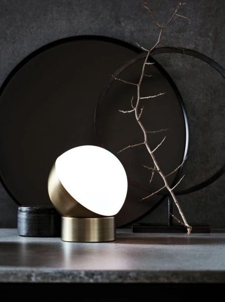 Moderne kugelförmige Tischleuchte mit Metallfuß in Messingoptik und dekorativer Lichtkugel auf einem Tisch als stimmungsvolles Wohnaccessoire.