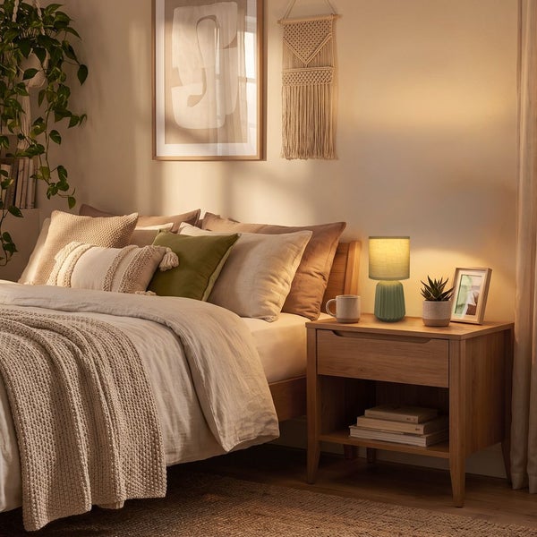 Gemütliches Schlafzimmer mit Holznachttisch und moderner Tischleuchte mit Textilschirm auf einer Kommode in einer warmen Wohnumgebung.