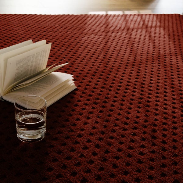 Strukturierter Teppichboden mit Waffelmuster, darauf ein aufgeschlagenes Buch und ein Glas Wasser.
