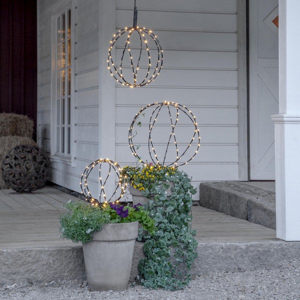 Szene mit drei leuchtenden Kugeln im Außenbereich, platziert in Pflanzgefäßen mit Pflanzen