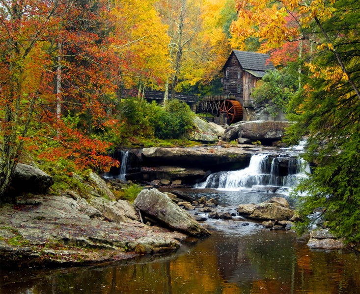 Historische Mühle am Wasserfall, umgeben von herbstlichen Bäumen