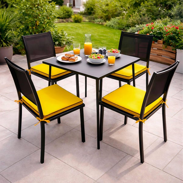 Modernes Gartenmöbel-Set bestehend aus quadratischem Metalltisch und vier Stühlen mit gelben Sitzkissen auf einer hellen Terrasse.