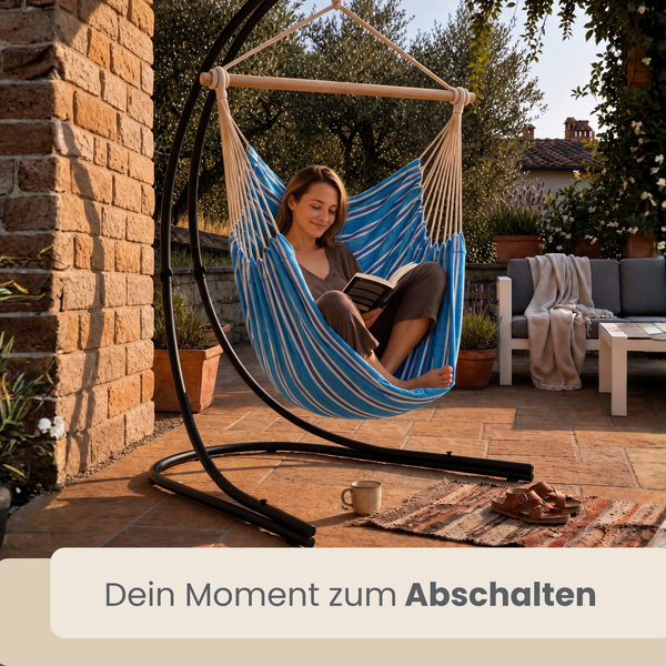 Frau liest ein Buch in einem gestreiften Hängesessel mit schwarzem Metallgestell auf einer Terrasse.