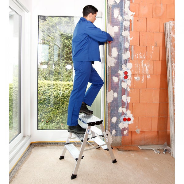 Handwerker auf einer Aluminium-Stufenleiter bei Renovierungsarbeiten an einer Ziegelwand.