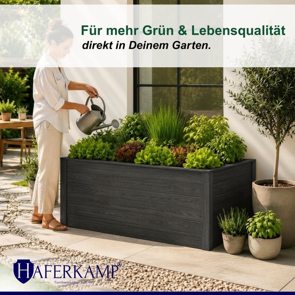 Eine Frau gießt Kräuter und Gemüse in einem großen, anthrazitfarbenen Hochbeet in Holzoptik auf einer Terrasse.