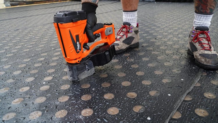 Handwerker verwendet einen Paslode Druckluftnagler auf einer genoppten Dachabdichtungsbahn im Außenbereich.