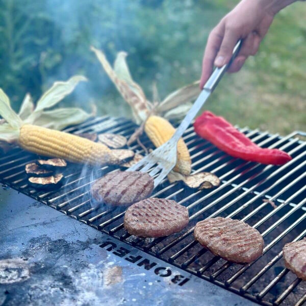 Burgerpatties, Maiskolben und Paprika werden auf einem BonFeu Grillrost mit einem Pfannenwender zubereitet.