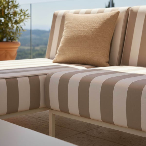Moderne Gartenlounge mit gestreiften Polstern und quadratischem Zierkissen auf einer hellen Terrasse.
