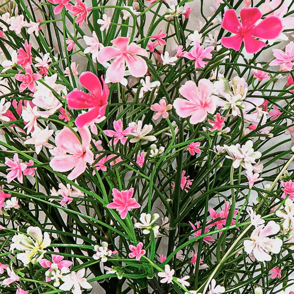 Künstliche rosa und weiße Blumen auf grünen Stielen.