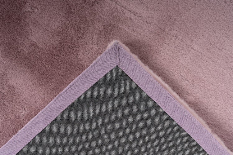 Altrosafarbener Teppich aus weichem Kunstfell, Nahaufnahme der umgeschlagenen Ecke mit strukturierter Rückseite und eingefasstem Rand.