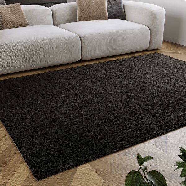 Moderner dunkler Teppich auf hellem Parkettboden im Wohnzimmer vor einem hellen Sofa.