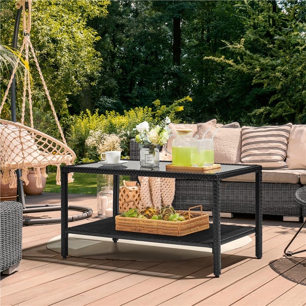 Schwarzer Garten-Couchtisch aus Polyrattan mit Glasplatte und Ablageboden, dekoriert auf einer Holzterrasse in einem hellen Garten.