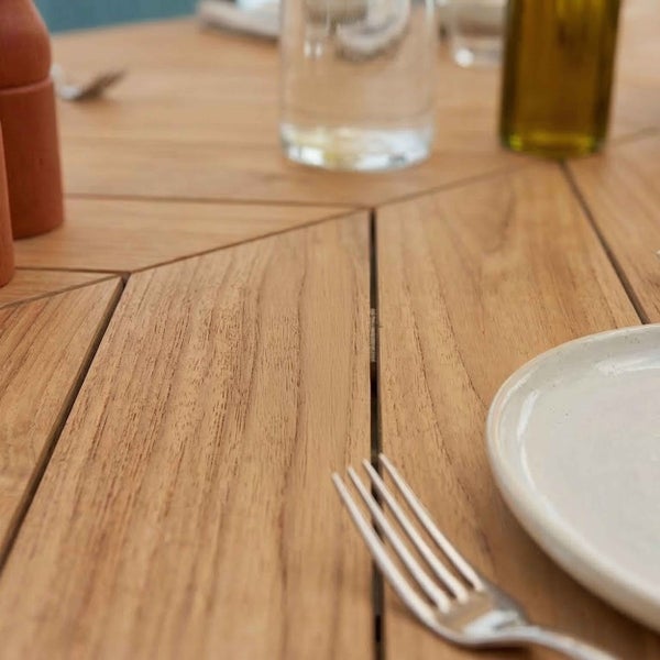 Nahaufnahme einer hölzernen Tischplatte mit Fischgrätenmuster aus Holzlatten, gedeckt mit Teller, Gabel und Gläsern.