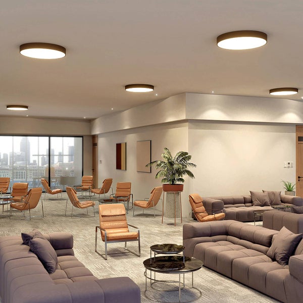 Helle moderne Lounge mit mehreren runden flachen LED Deckenleuchten braunen Sofas und Ledersesseln