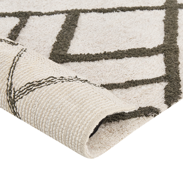 Nahaufnahme eines Hochflor-Teppichs mit geometrischem Rautenmuster und umgeschlagener Ecke, die die Rückseite zeigt.