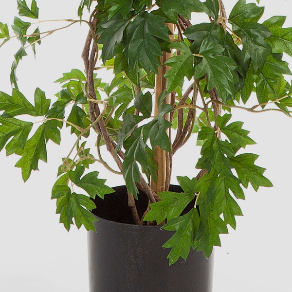 Künstliche Pflanze mit gezackten Blättern und braunen Zweigen im schwarzen Topf.