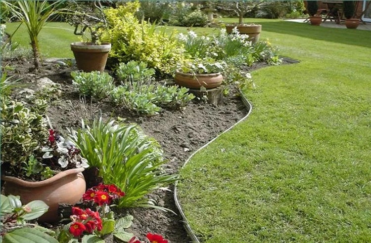 Geschwungene Rasenkante aus Metall trennt ein bepflanztes Gartenbeet mit Terrakotta-Töpfen von einer gepflegten grünen Rasenfläche.