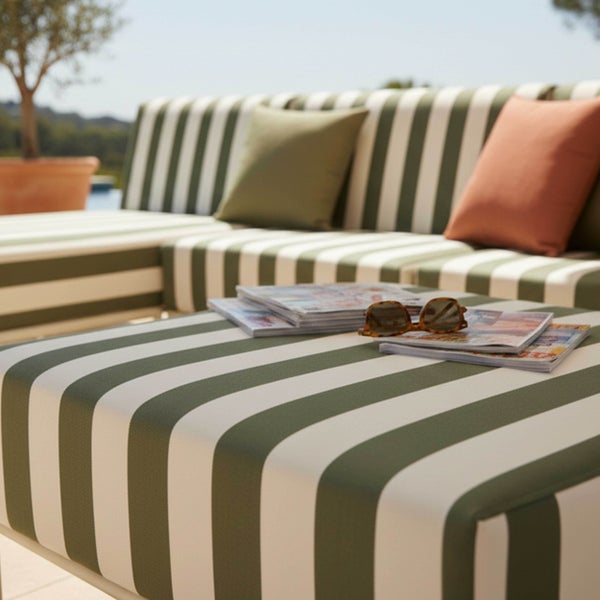 Gestreifte Outdoor-Lounge-Möbel bestehend aus Sofa und Hocker mit grünen und orangefarbenen Dekokissen auf einer hellen Terrasse.