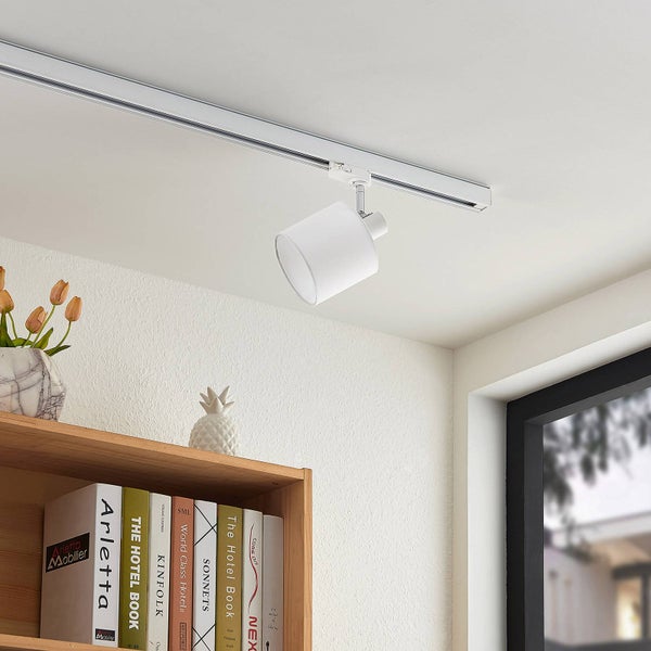 Weißes Schienensystem mit einem zylindrischen Strahler an einer Zimmerdecke über einem Holzregal mit Büchern.