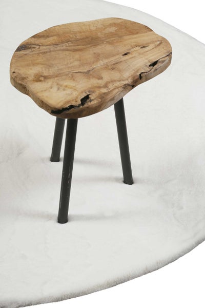 Beistelltisch aus massivem Holz mit unregelmäßiger Baumscheibe und drei schwarzen Metallbeinen auf einem weißen Teppich.