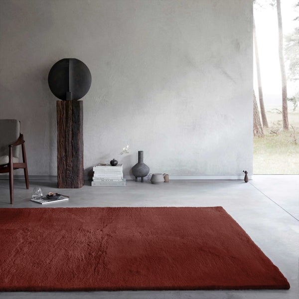 Moderner roter Hochflor-Teppich in einem hellen, minimalistischen Wohnraum mit Betonwand und dekorativen Skulpturen.