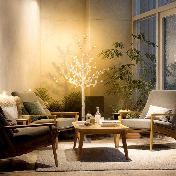 Wohnzimmer mit beleuchtetem Birkenbaum, Sesseln und Holztisch auf Teppich