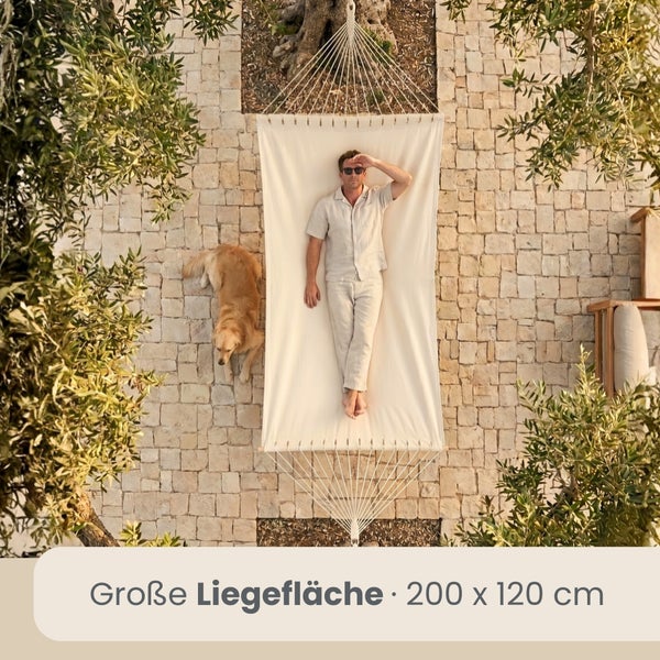 Große weiße Hängematte mit 200 mal 120 Zentimeter Liegefläche, in der eine Person auf einer Steinterrasse im Garten liegt.