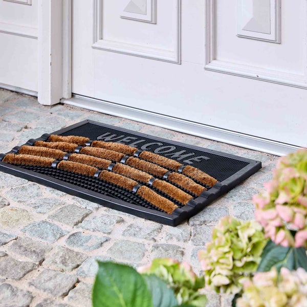 Fußmatte mit Kokosborsten und Willkommensaufschrift vor einer Haustür