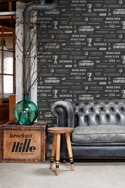 Wohnszene mit grauer Couch, Holzhocker und Dekoration auf einer Holzkiste vor einer gemusterten Tapete