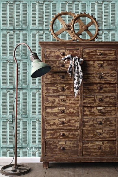 Vintage-inspirierte Wohnraumszene mit Kommode, Lampe und dekorativen Elementen vor einer Tapete mit Fensterladenmotiv