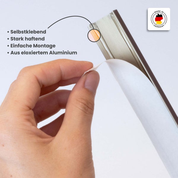 Selbstklebendes Profil aus eloxiertem Aluminium, Hand zieht Schutzfolie vom Klebestreifen ab, Siegel Made in Germany.