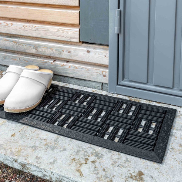 Fußabstreifer aus Gummi vor einer Haustür mit Holzverkleidung und Clogs.