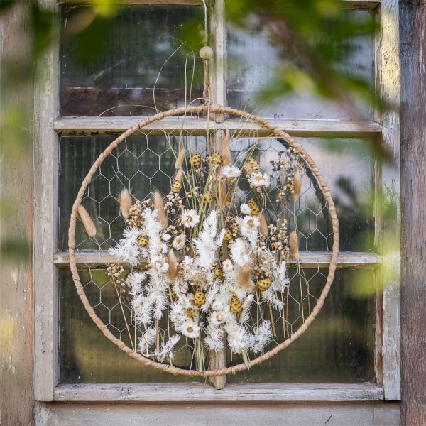 Dekorativer Trockenblumenkranz mit Drahtgeflecht vor einem Fenster