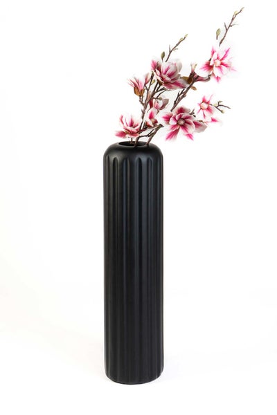Hohe schwarze Vase mit vertikalem Rillenmuster und künstlichen rosa Magnolienblüten.
