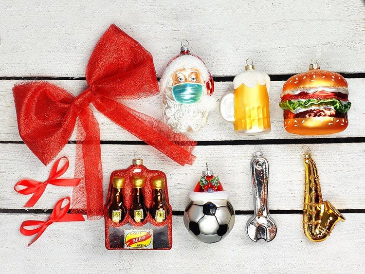 Set mit ausgefallenen Weihnachtskugel Anhängern aus Glas in verschiedenen Formen wie Bier, Burger, Fußball und Saxophon auf Holzuntergrund.