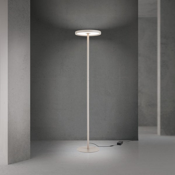 Moderne LED Deckenfluter Stehleuchte mit rundem Leuchtkopf und schlankem Standfuß in minimalistischem Design vor einer Betonwand.