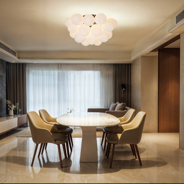 Modernes Esszimmer mit einer großen Deckenleuchte aus weißen Glaskugeln, einem ovalen Marmortisch und beigefarbenen Polsterstühlen.