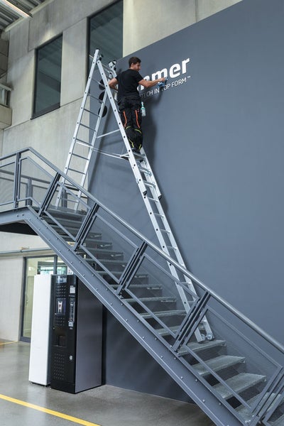 Mann reinigt mit einer Aluminium Mehrzweckleiter eine Wand auf einer Treppe.