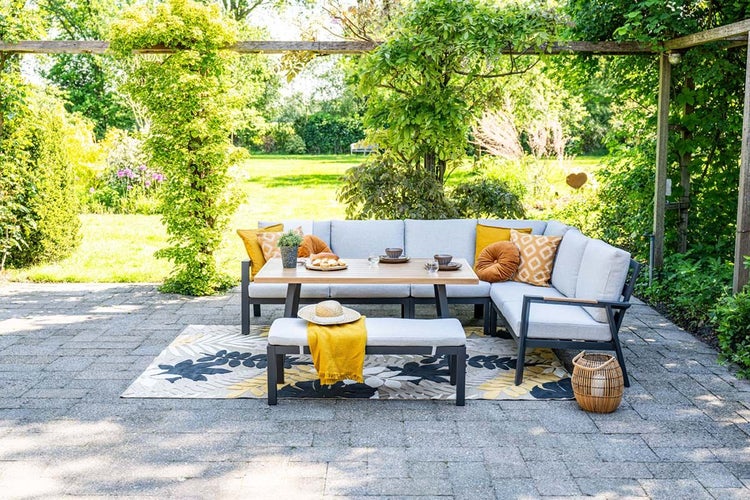 Modernes Garten-Lounge-Set aus Metall mit hellgrauen Polstern, Holztisch und Bank auf einer sonnigen Terrasse im Grünen.