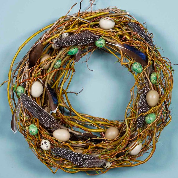 Dekorativer Türkranz aus Zweigen mit Federn und Eiern für Ostern