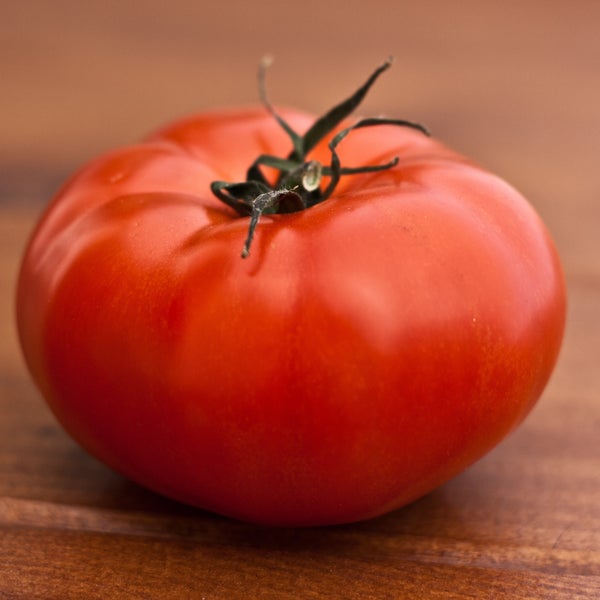 Große, reife Fleischtomate mit grünem Stielansatz auf einer Holzoberfläche.