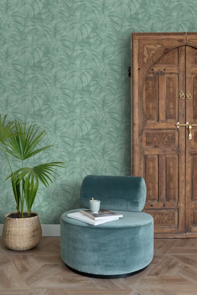 Wohnszene mit Monstera-Blatt-Tapete, Ottoman, Holztür und Zimmerpflanze im Topf.