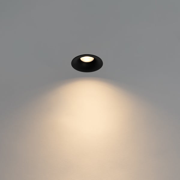Schwarzer runder Einbaustrahler mit warmweißem Lichtkegel an der Wand.