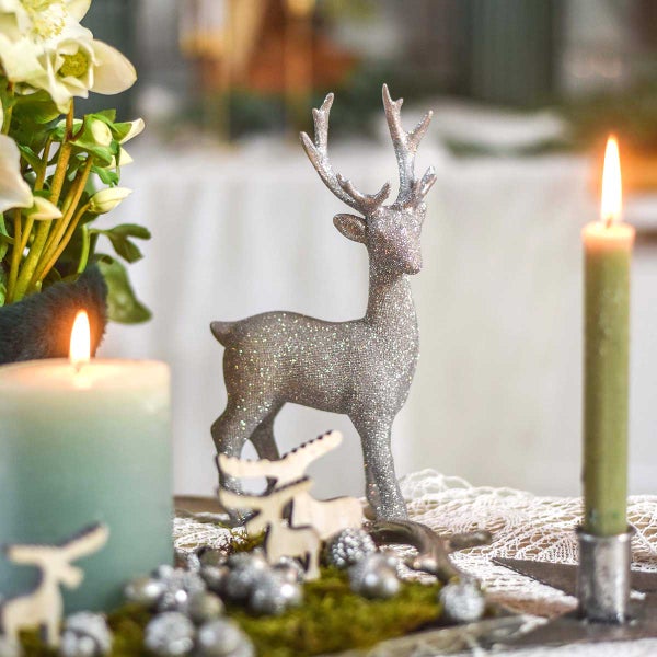 Festliche Dekoration mit einem glitzernden Hirsch, Kerzen und floralen Elementen für eine weihnachtliche Atmosphäre.